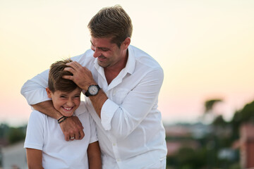 Fototapeta premium Father And Son Laughing Together On Rooftop Balcony Overlooking Sea At Sunset Family Moment