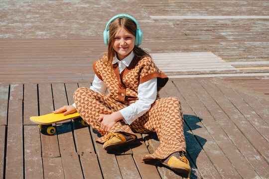 Girl sits on wooden embankment listening to music in summer