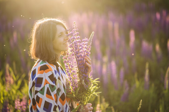 Smiling woman in sweater holds lupine bouquet in field at sunset