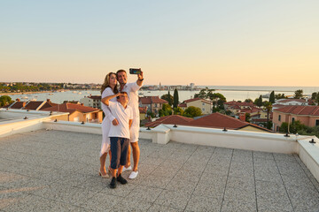 Obraz premium Family Taking Selfie On Rooftop Terrace With Sea View At Sunset During Summer Vacation