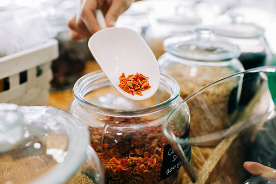 Hand scooping dried food into glass jar at zero waste store