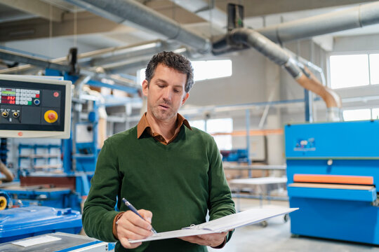 Portrait of carpenter standing in production hall with ring binder in hands