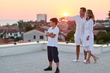 Obraz premium Family on Rooftop Balcony Watching Sunset Over Sea View From Coastal Town Terrace
