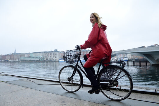 Denmark, Copenhagen, happy woman riding bicycle at the waterfront in rainy weather