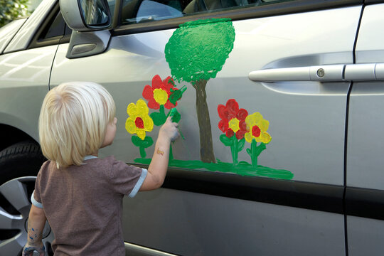 Child finger painting a flower on a car door causing a disaster