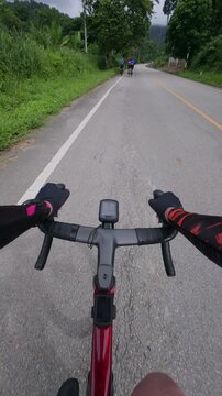 First-person point of view of a road cyclist riding along a quiet countryside road with a small group of cyclists ahead. Surrounded by lush tropical forest, peaceful nature, and winding asphalt road, 