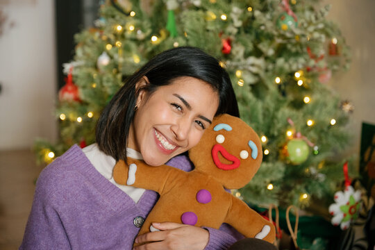 Smiling woman hugs a gingerbread man indoors by a Christmas tree