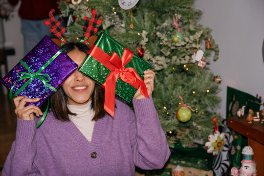 Smiling woman holds wrapped Christmas present in front of her face