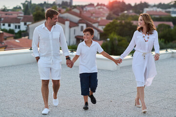 Obraz premium Family Walking On Rooftop Terrace At Sunset Holding Hands During Summer Vacation