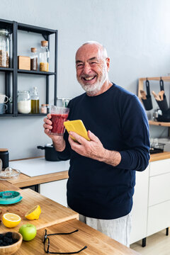 Senior man holding mobile phone and smoothie at home