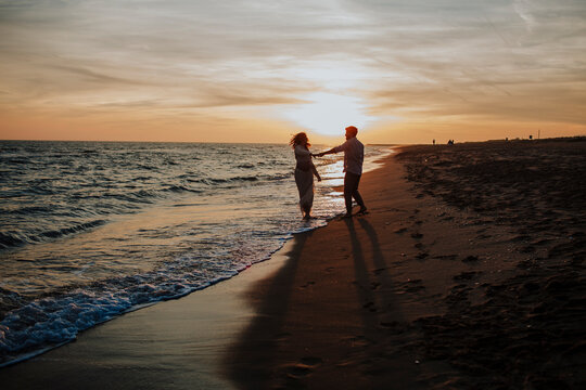 Expecting couple dancing on the beach at sunset