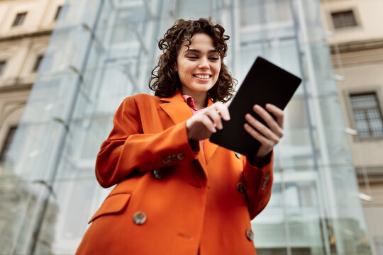 Smiling woman using tablet PC in front of building