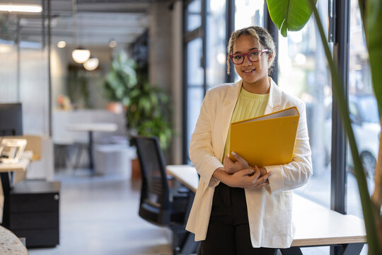 Smiling young businesswoman standing with file folder at office