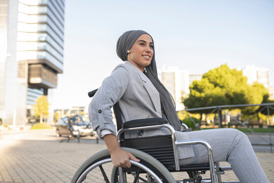 Smiling disabled woman sitting on wheelchair at footpath