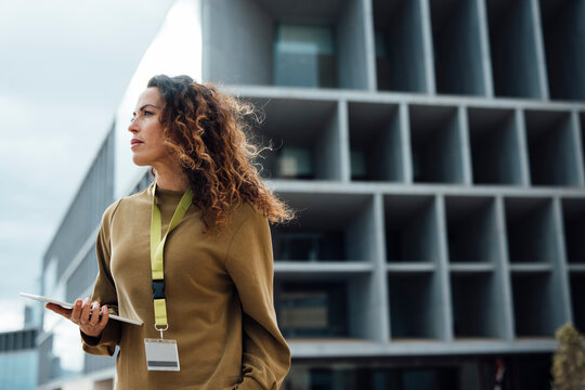 Contemplative businesswoman with tablet PC in front of office building