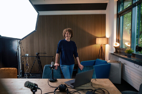 Smiling presenter standing amidst chair at radio station