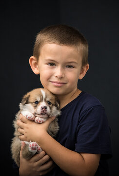 cute young boy cuddling a baby Pembroke Welsh Corgi puppy against a dark background.
