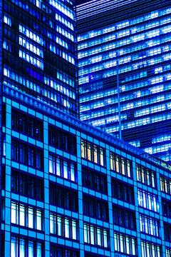 Abstract low-angle perspective of towering corporate skyscrapers in Tokyo at night with geometric blue windows.