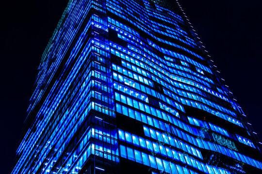 Low-angle view of a monolithic modern skyscraper in Tokyo at night with glowing blue window grid patterns.