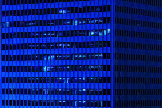 Minimalist abstract view of modern skyscraper facade at night with dense blue lighting and glass windows.