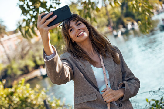 A smiling woman takes a selfie with a phone in the park