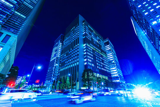 Wide-angle night cityscape of Tokyo financial district with fast-moving traffic light trails and illuminated skyscrapers.