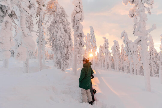Young woman with snowboard standing on snow-covered field during sunrise