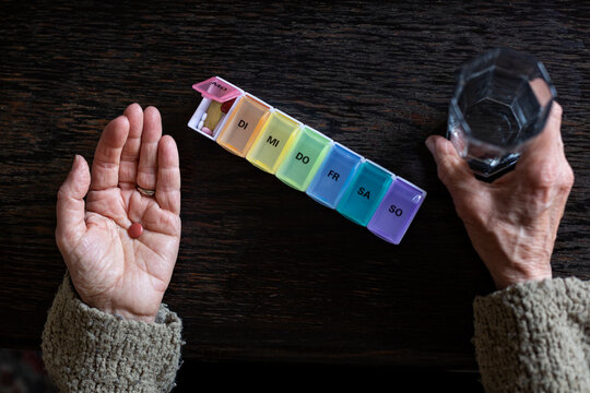 Senior woman taking medicine, water glass and pill organiser