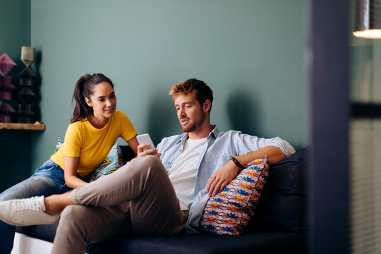 Young couple sitting on the couch at home looking at smartphone