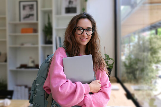Young student wearing eyeglasses holding laptop at cafe