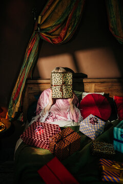 Woman in bed hiding face behind a birthday gift in the morning
