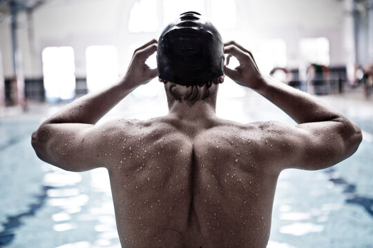 Swimmer in indoor pool putting on swimmming goggles