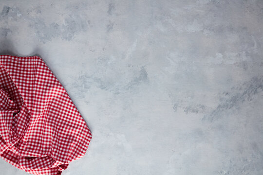 Top view of a red and white checkered kitchen napkin on a textured gray background, empty mockup template with copy space for food photography and design layout.