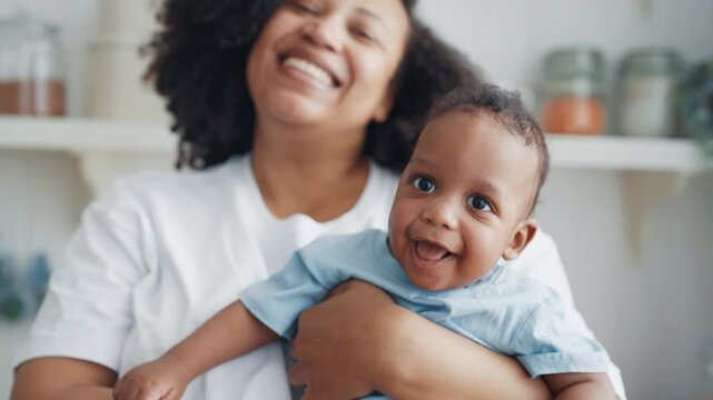 Motherhood and childhood, portrait of african woman holding baby and smiling. Charming smile of little child in mother hands, portrait in cozy home interior, emotions and good mood, happy family