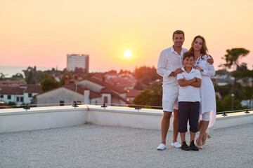 Obraz premium Happy Family On Rooftop Balcony At Sunset With Sea View Over Coastal Town