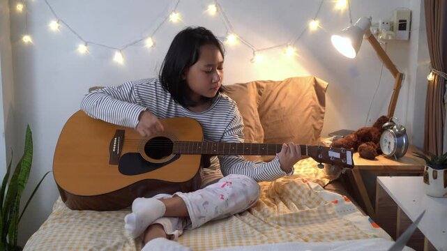 Young Girl carefully practicing chords on an acoustic guitar in Cozy Bedroom at Home	