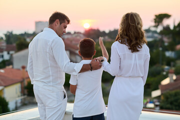 Obraz premium Family Watching Sunset From Rooftop Balcony With Son Overlooking Seaside Town Together
