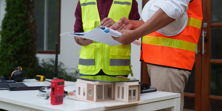 Cropped shot of architects reviewing blueprints over house model at construction site