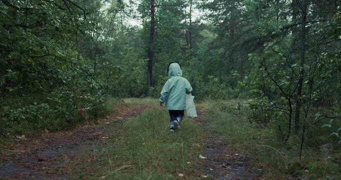 Little child in hooded jacket running along path in a dense green forest