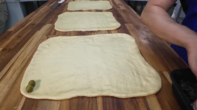 Baker placing green olives on raw dough for ham bread