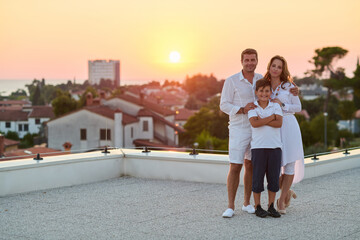 Obraz premium Happy Family On Rooftop Terrace At Sunset With Sea View During Coastal Vacation