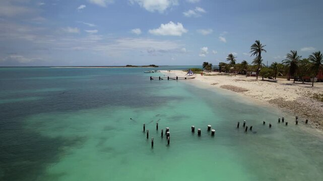 Low flyover above crystal clear Caribbean sea with old wooden pillars near a rustic nature reserve shore in Dos Mosquises island in Los Roques Venezuela