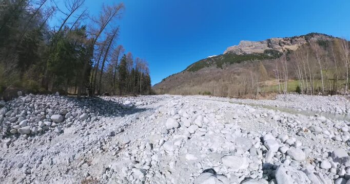 Expansive aerial 360-degree footage showcasing the rugged beauty of Maloja Pass in Switzerland, with a rocky valley floor leading to towering mountains under a pristine blue sky.
