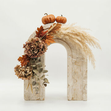 Minimalist autumn floral arrangement on stone arch, elegant fall centerpiece with dried pampas grass and pumpkins, rustic harvest home decor