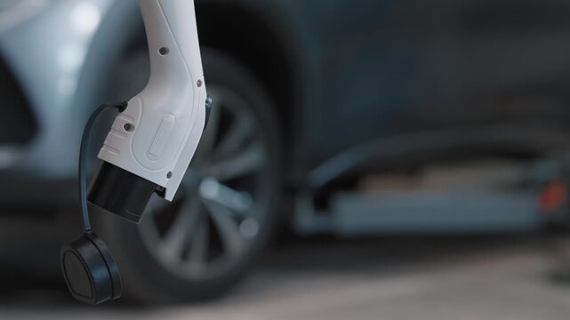 White charging cable hooks into electric car's port. Vehicle rests quietly, plugged in. Modern energy replaces fossil fuels. Clean transport future arrives. Urban or home charging station