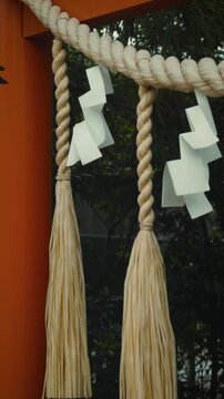 Close-up vertical shot of a traditional Shimenawa sacred rope and white Shide paper streamers swaying in the wind at a Japanese shrine