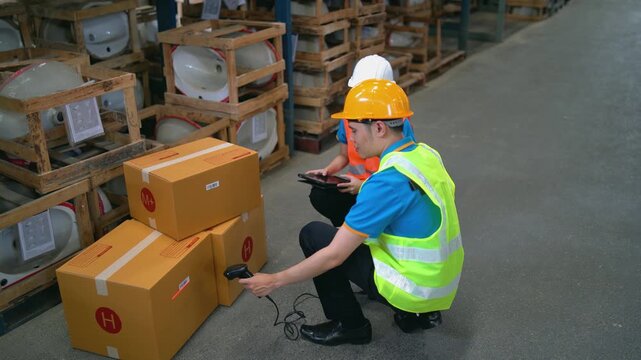 Warehouse worker scanning barcode on cardboard box during inventory check with clipboard and safety gear in storage facility with stacked items on pallets