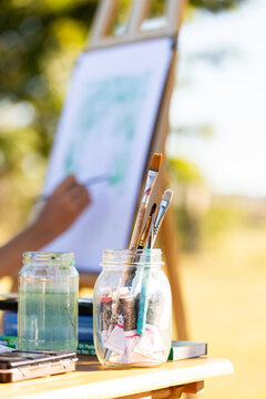 Paint brushes in jar beside artist working on live artwork at event