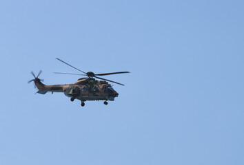 Fototapeta premium Military camouflage transport helicopter flying in the clear blue sky during a defense aviation mission with spinning rotors in active high flight.