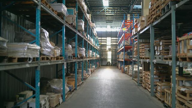 Industrial warehouse interior with metal shelving units filled with cardboard boxes and wrapped packages on wooden pallets, bright spacious storage facility aisle